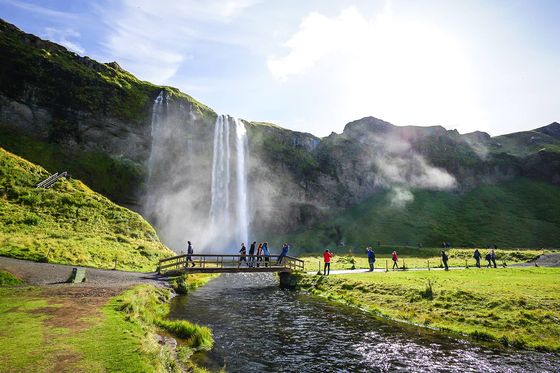 People walking across a bridge with a tall waterfall in the background