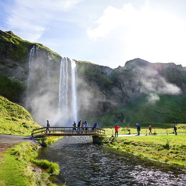 People walking across a bridge with a tall waterfall in the background