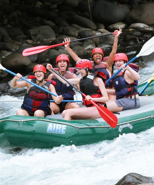 A group of people wearing helmets and life jackets holding paddles in a raft on a river