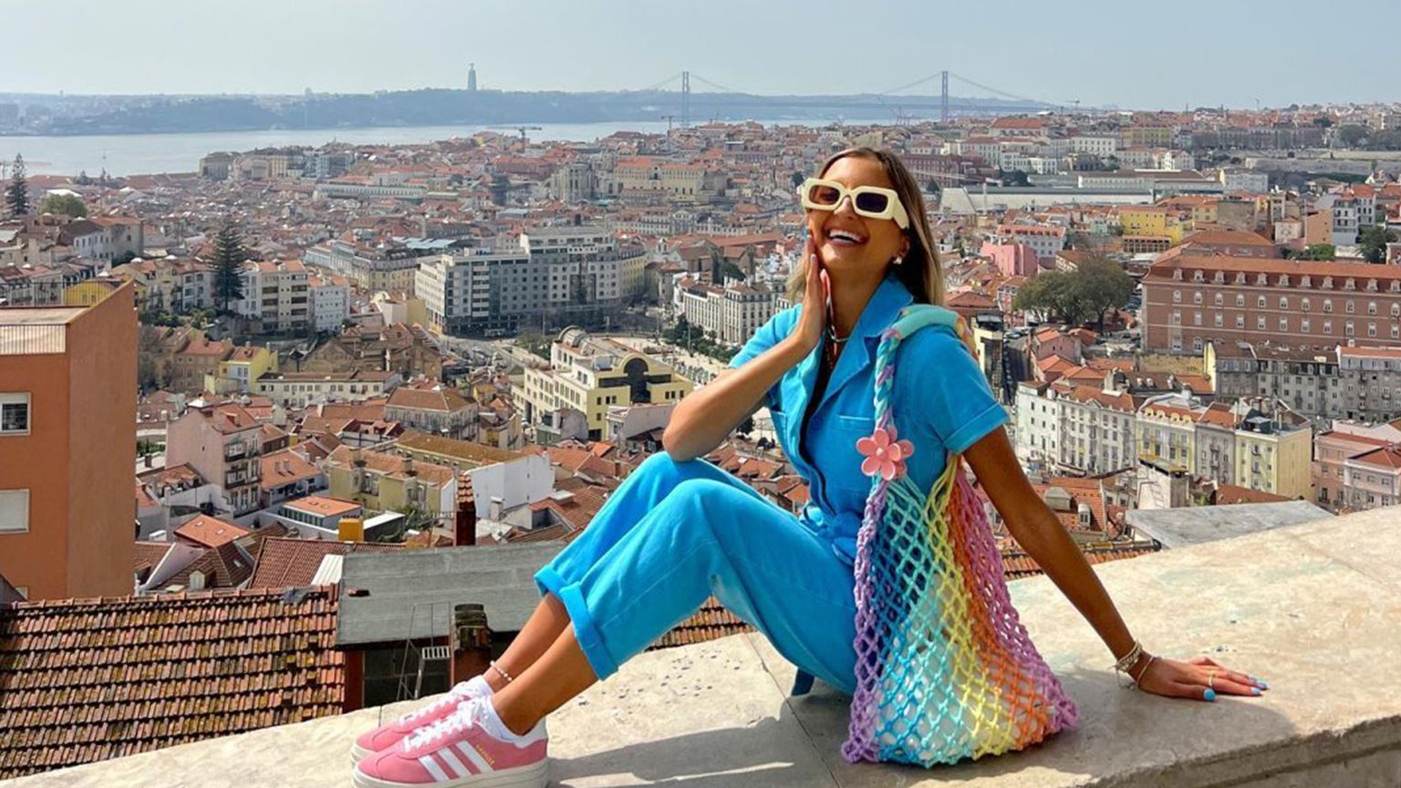 A man standing on a red dirt trail looking out at a view of mountains and valleys
