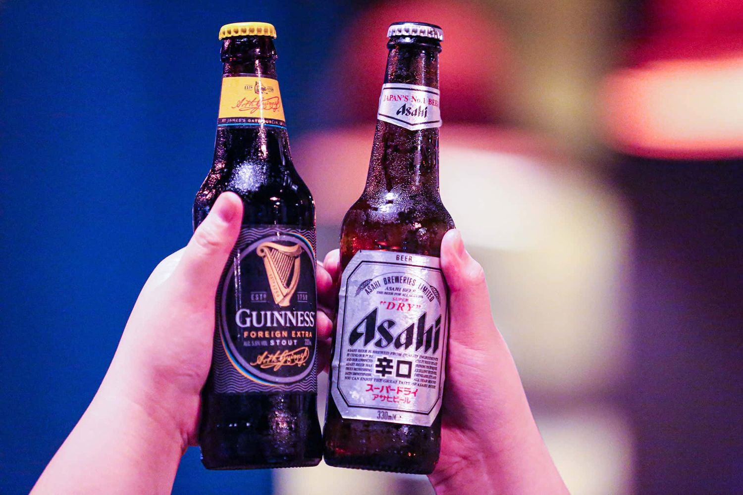 Two beer bottles, one Guinness and one Asahi, being held in the air.