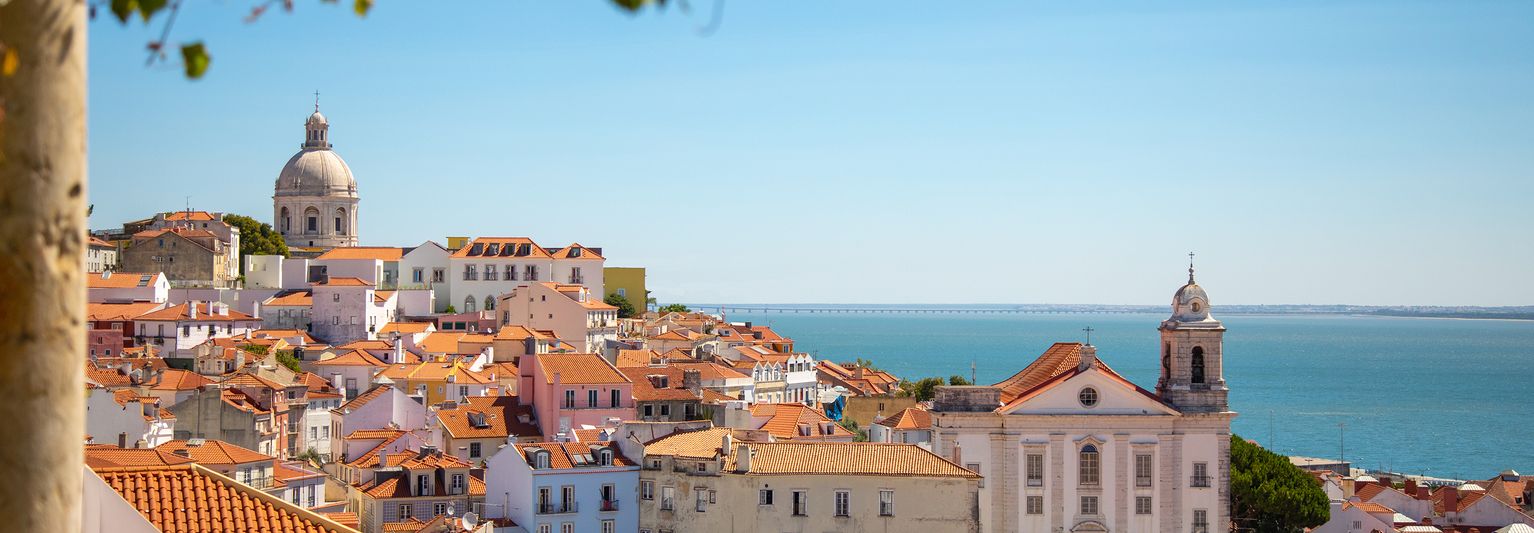 A photo of Lisbon orange brick rooftops in the foreground with the ocean in the background.