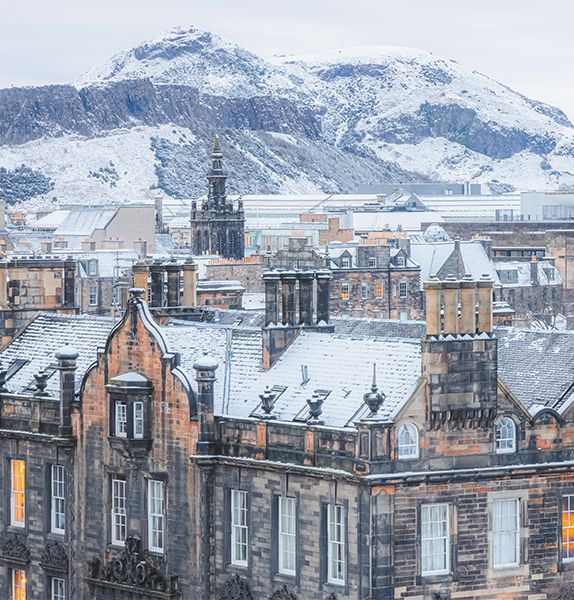 Several rows of unique brick buildings with dark discoloration on the red bricks and a snow covered mountain in the background