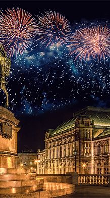 A grand statue of a figure riding on a horse nearby a huge ornate mansion during nighttime with fireworks covering the night sky