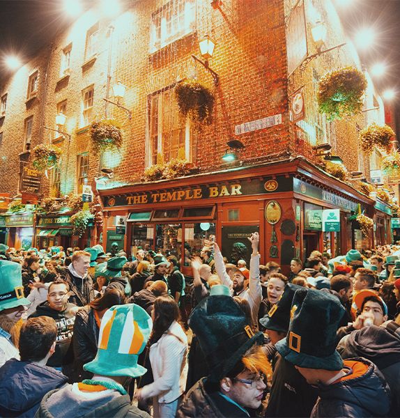 A building during nighttime with many people surrounding the building and signs on the building that read "The Temple Bar"
