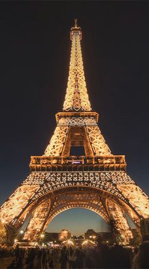 A bottom-up view of the Eiffel Tower lit up against the dark night sky with several people standing around the base of the tower