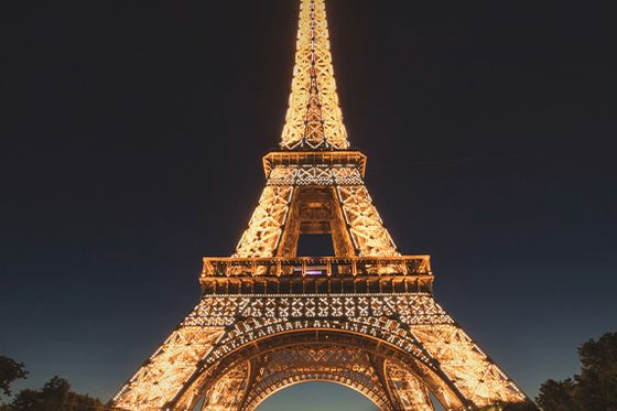 A bottom-up view of the Eiffel Tower lit up against the dark night sky with several people standing around the base of the tower