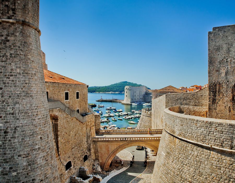 tan stone walls in dubrovnik leading down to a marina filled with sail boats