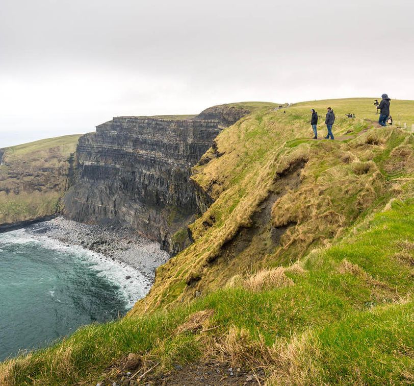 people walking along the cliffs of moher in ireland on cloudy day