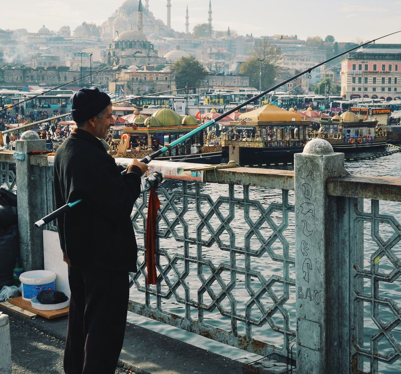 man fishing on a bridge in istanbul with the blue mosque in the background