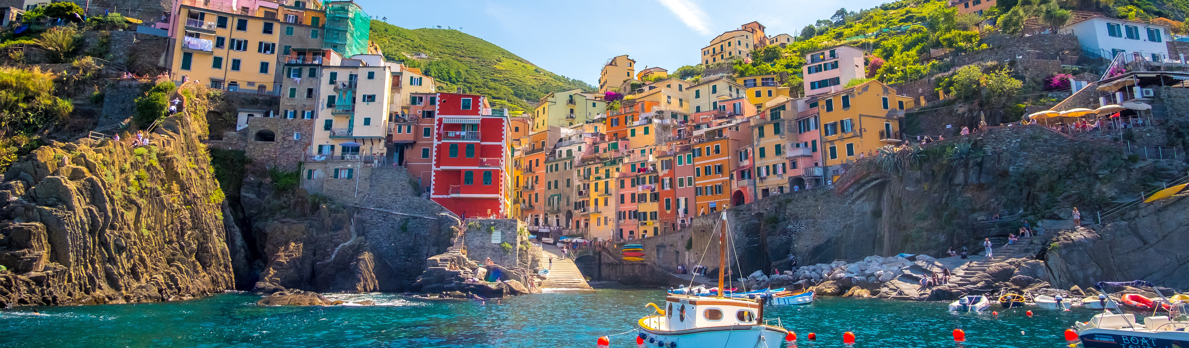 boats in the marina with people walking along wall in cinque terre italy