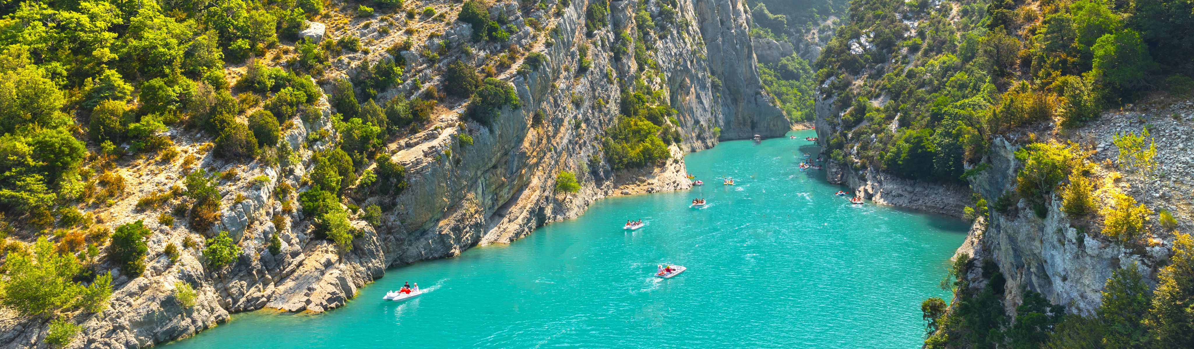 people in floats boating down teal blue river in the verdon gorge in france