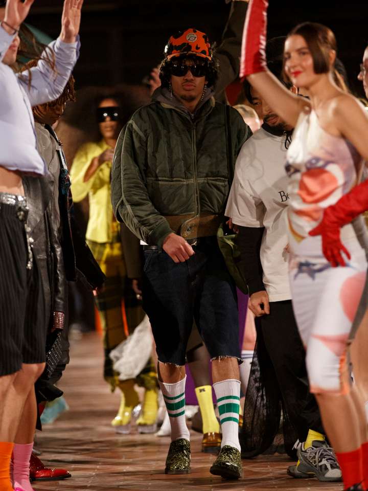 A man walking the runway and a lot of models are walking and dancing around him. all wearing happy socks. 