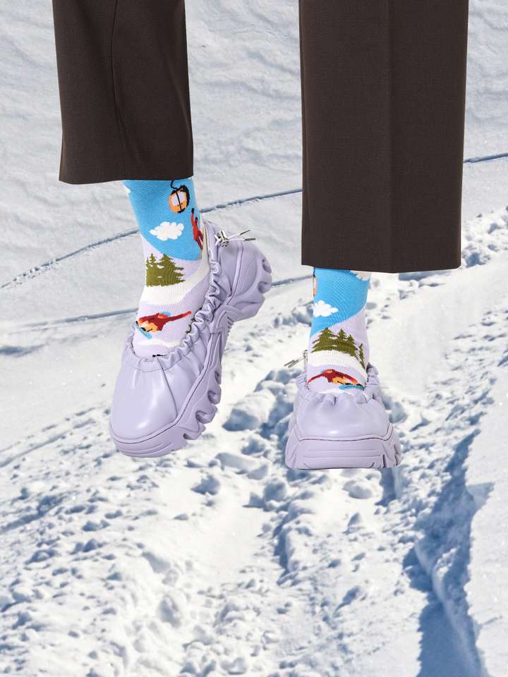 Ski slopes landscape with a pair of legs superimposed on top wearing winter style Happy Socks.