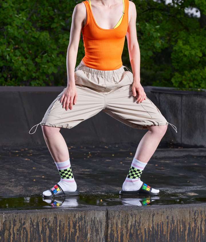 A person standing with their legs spread atop a concrete block. The person is wearing white Happy Socks with a black and green checker pattern below the cuff.