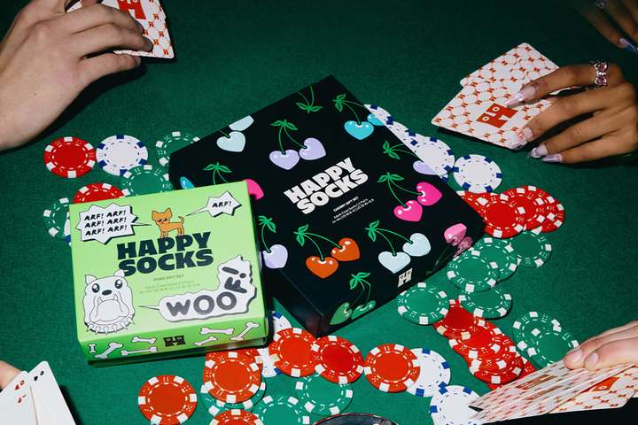 Eine große gepunktete Geschenkbox mit drei Paar Socken rechts davon auf grauem Hintergrund