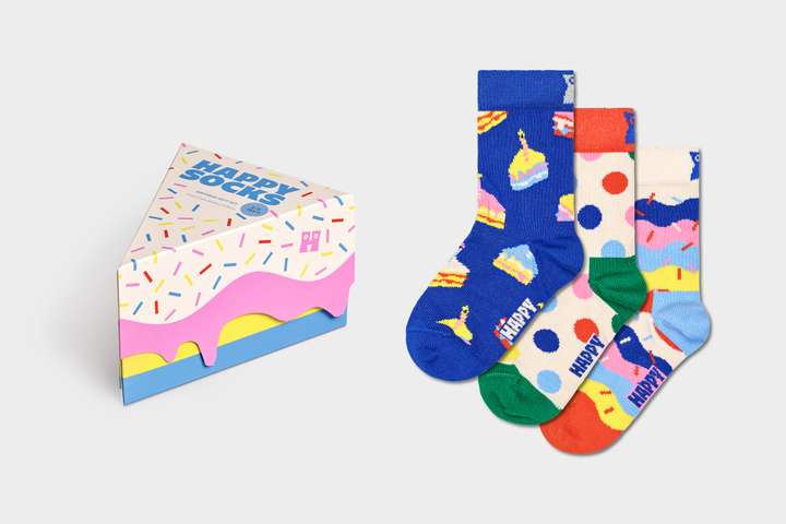 A birthday cake slice shaped gift box pictured besides three kinds of different birthday Happy Socks. 