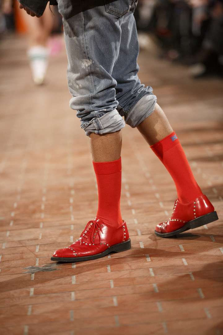 A person walking on the runway wearing red solid socks from happy socks, matched with red shoes 