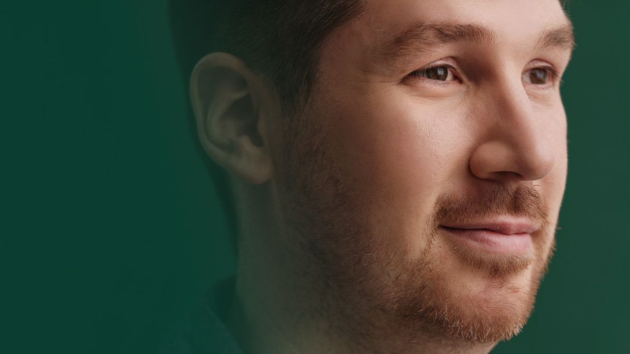 Le gros plan d'un homme, devant un fond vert. Il sourit et regarde vers l'avenir.