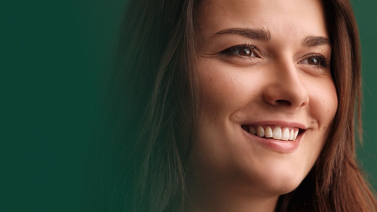 Une femme en grand plan, devant un fond vert, regarde vers l'avenir et sourit.