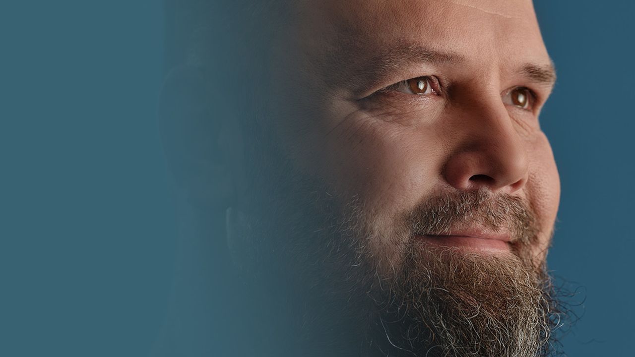 A bearded man looks upward against a gradient blue background.