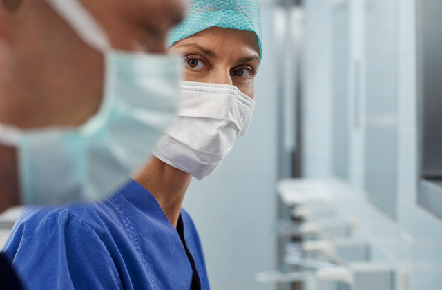 Medical professionals wearing surgical masks and scrubs in a sterile hospital environment.