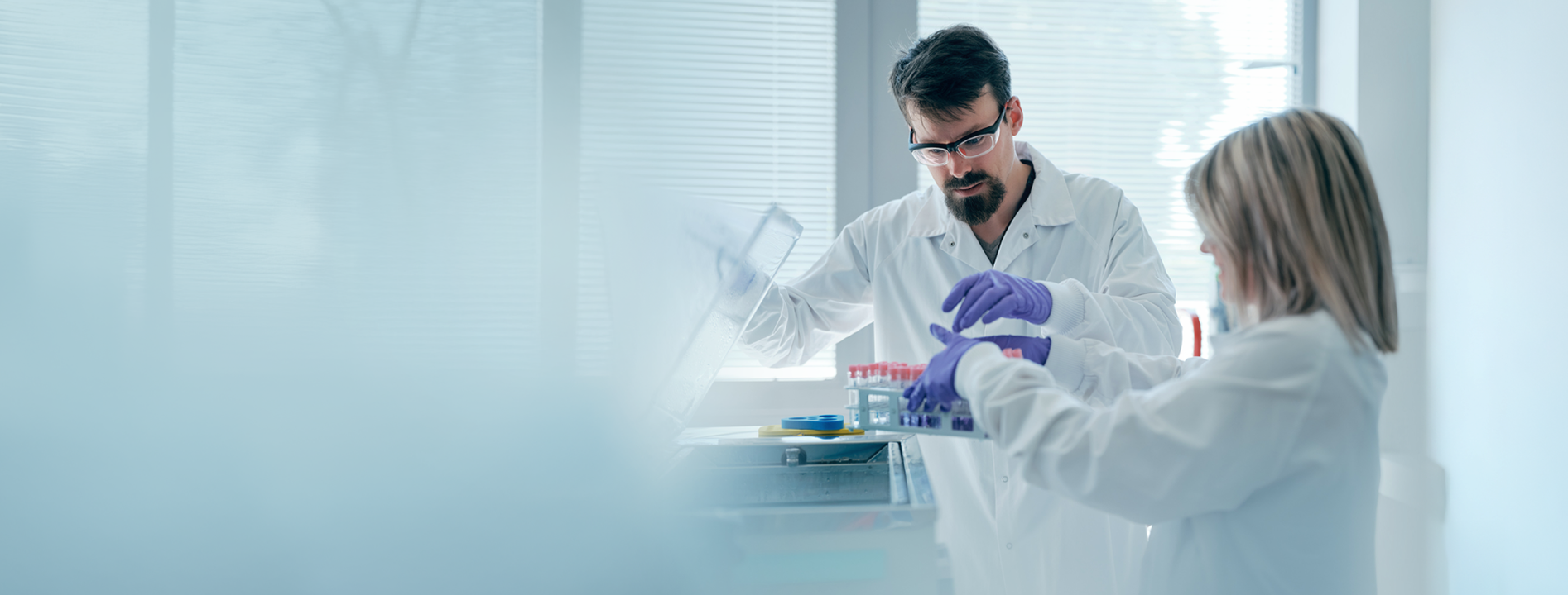 Two scientists in lab coats, one man and one woman, examining test tubes in a bright laboratory.