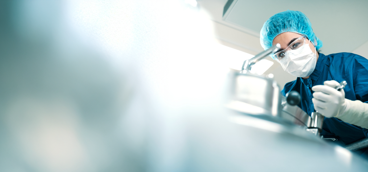 Scientist wearing protective clothing, mask, and gloves working with laboratory equipment in a sterile environment.