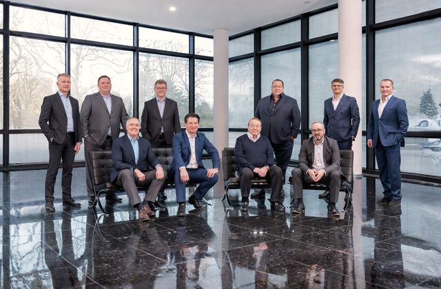 Octapharma executive board, some seated and others standing, pose in a modern room with large windows.