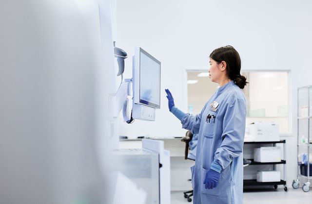 Ein Labortechniker in blauer Arbeitskleidung und Handschuhen bedient einen Touchscreen-Monitor in einer modernen Laborumgebung.