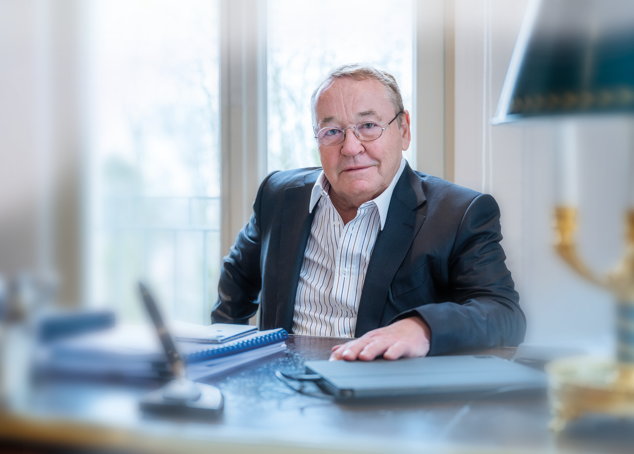 Wolgfang Marguerre sits at a desk with papers and a lamp, near a large window.