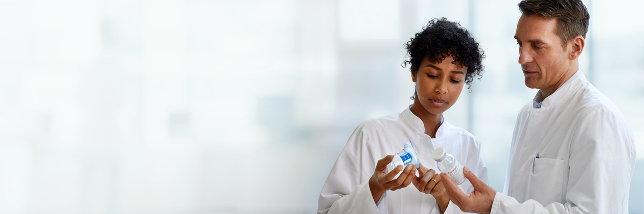 Two HPCs in white coats discuss medications, examining prescription of fibryga against a blurred background.