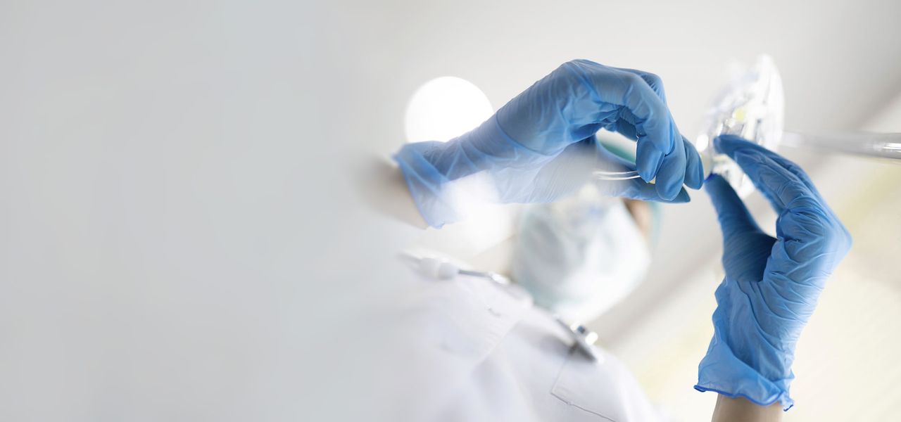 Medizinischer Fachmann mit Handschuhen und Maske untersucht einen Infusionsbeutel in einer hellen klinischen Umgebung.