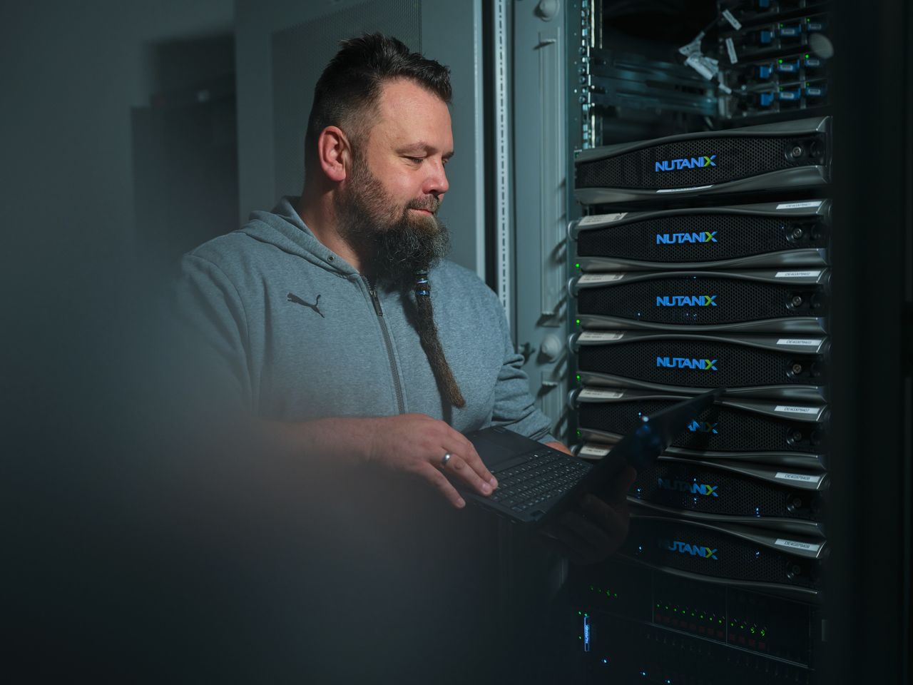 A person in a gray hoodie works on a laptop in a server room filled with Nutanix server racks.