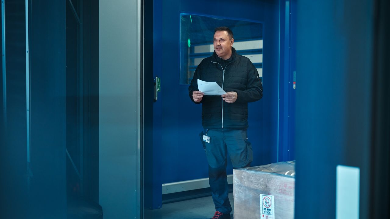 A man standing by in front of an industrial door holding a sheet of paper in his hand