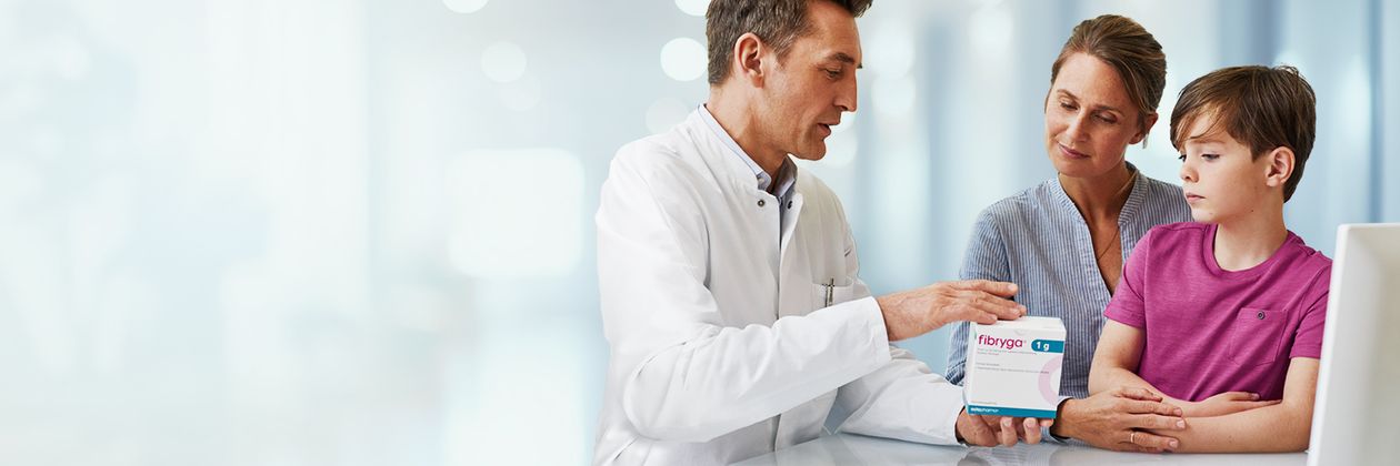 A doctor in a white coat explains fibryga to a woman and a child, sitting at a desk in a bright, clinical setting.