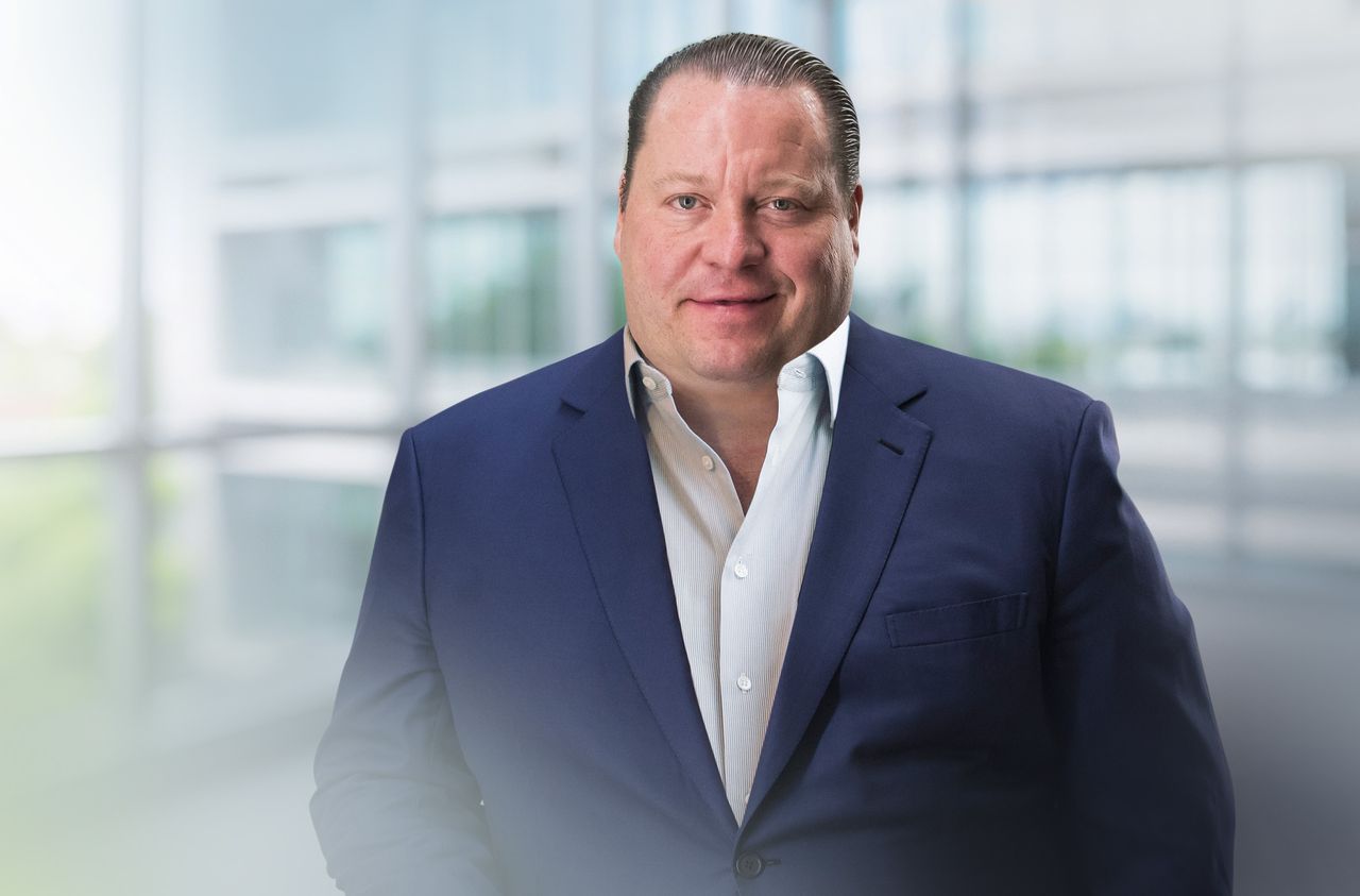 Tobias Marguerre in a blue suit and white shirt in a bright, modern office setting with large windows.