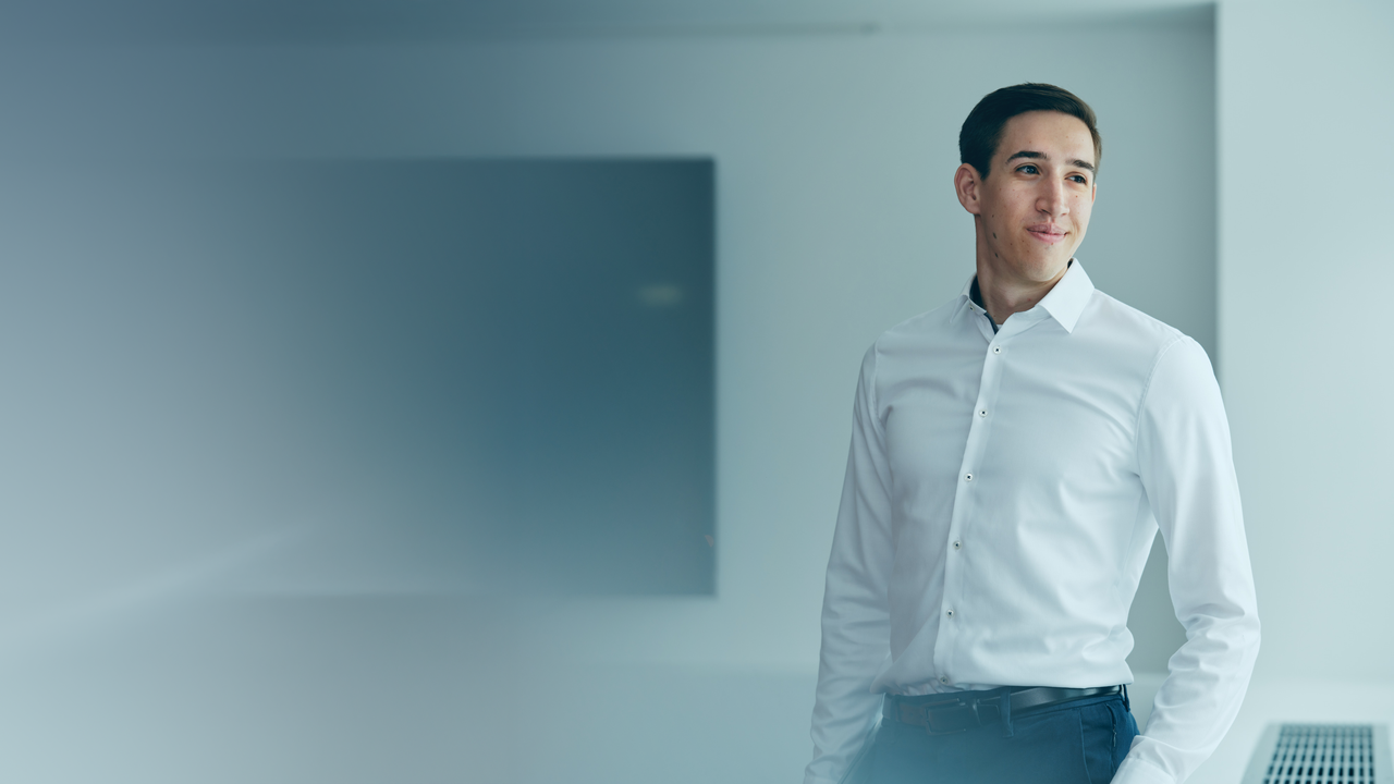 Portrait von Daniel Tamas auf dem er in einem Büro steht und nach rechts blickt. Daniel trägt ein weißes Hemd.