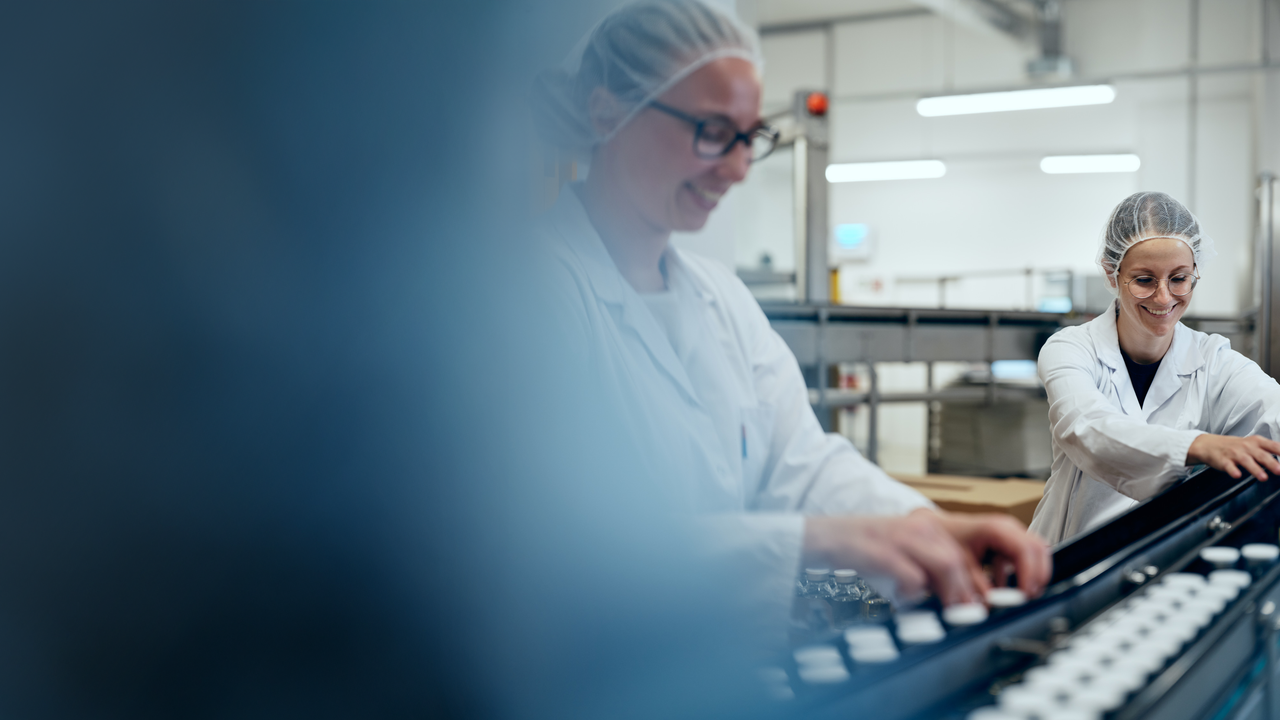 Bild von Anna Kämpf auf dem sie Octapharma Produkte auf einem Fließband kontrolliert. Anna trägt einen weißen Kittel und ein Haarnetz.