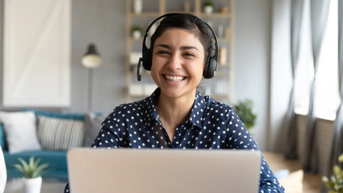 A smiling woman with a headset on behind a laptop