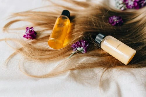 a strand of hair on a white sheet - with purple flowers and hair product placed on top.