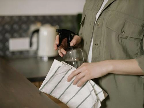 Person cleaning a counter with a spray bottle and striped cloth in a kitchen setting.