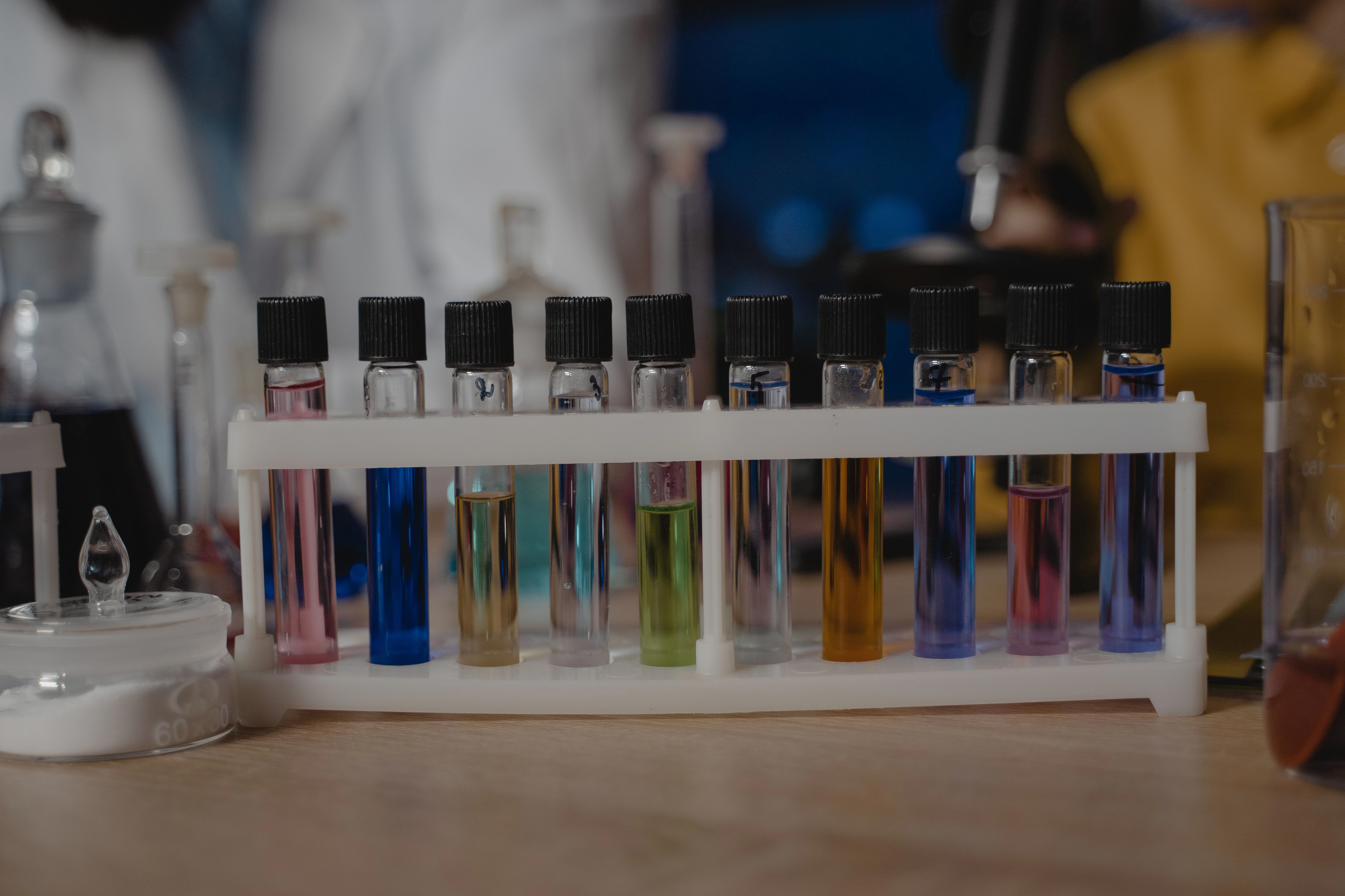 Laboratory test tubes containing coloured liquid samples in a rack, representing efficacy testing of biocidal and disinfectant products against bacteria and fungi under EN 1276 and EN 13697 standards.