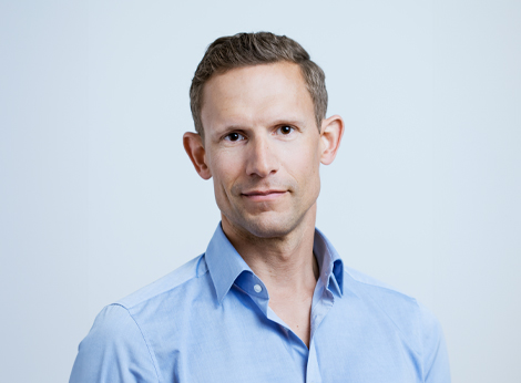 Dr Philipp Mayr, smiling at the camera in front of a blue background