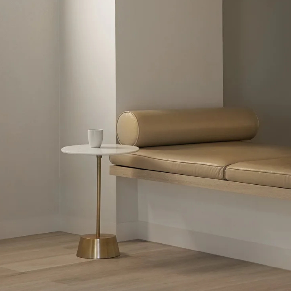 Holism Retreat - Small gold and white circle table with glass on it and a comfortable tan couch built into wall