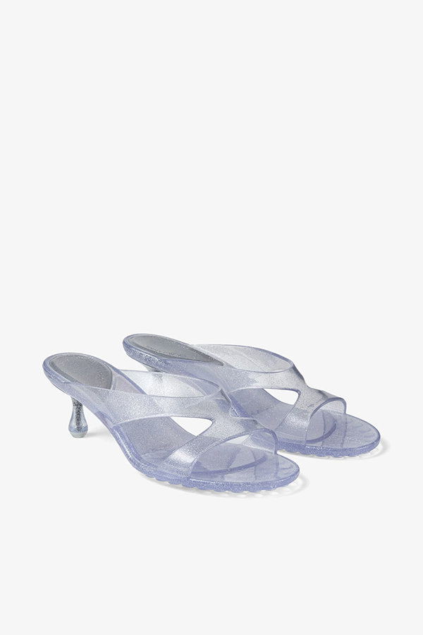 The Jelly Drop mule sandal in silver glitter TPU offers a translucent finish infused with fine shimmer, achieved through advanced moulding technology. The slip-on silhouette features fluid, intersecting straps that cross over the foot and a softly rounded open toe. Set on a 50mm sculpted drop heel, the tonal TPU sole is finished with textured grip detailing for stability.