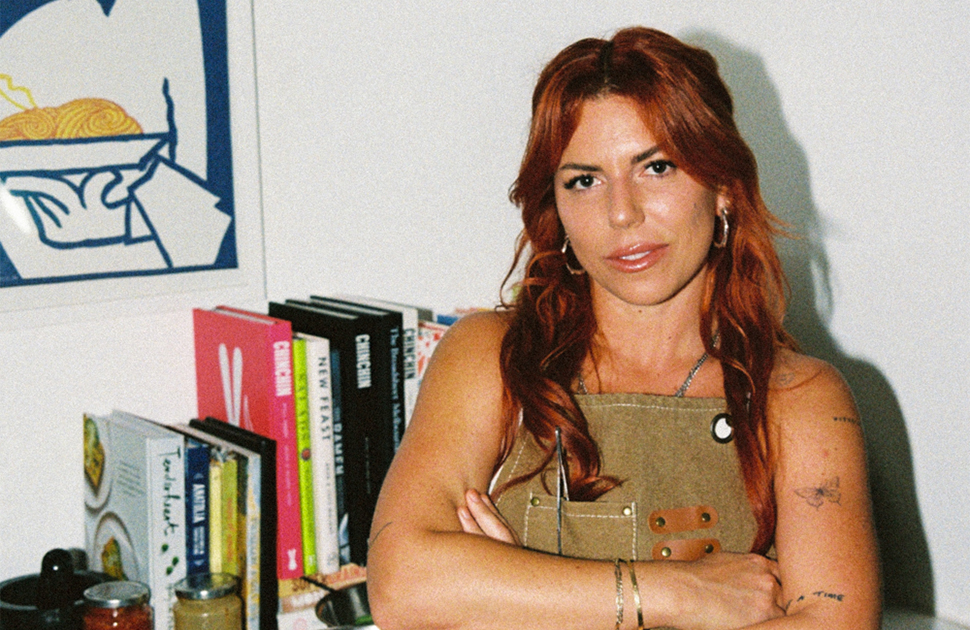 Lucy Rosenberg stands in front of a white wall and table with books