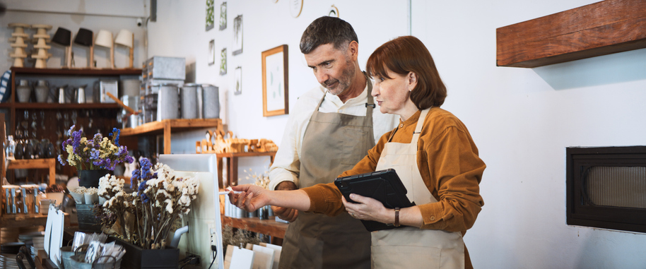 two employees at small business retail shop. Discuss talk using digital tablet, computer
