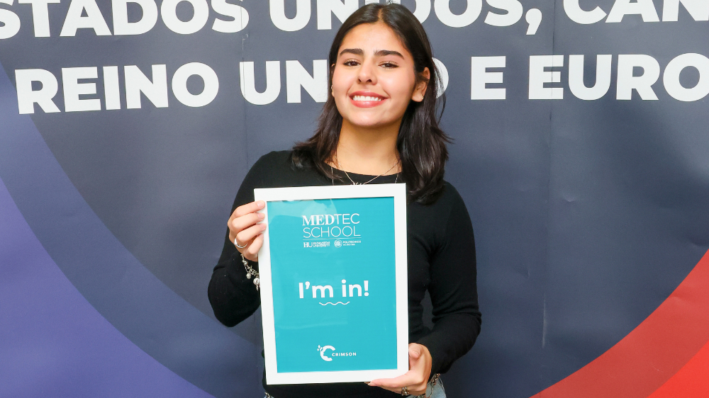 Aluna da Crimson Education sorridente segurando cartaz 'I'm in!' da MedTec School, aprovada em faculdade de medicina na Europa