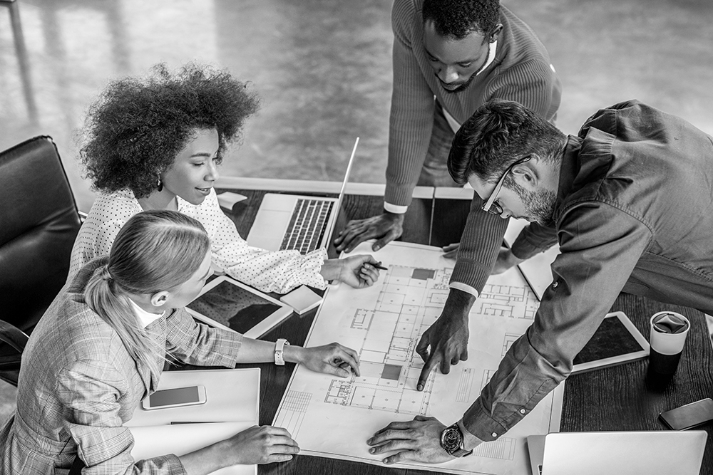 Coworkers in office looking over blueprints on a table.